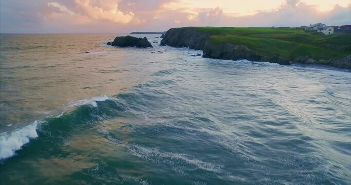 Aerial: Flying over ocean and rocky coastline at sunset. Annestown beach, Tramore, Ireland