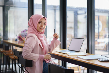 Confident muslim business woman working on laptop computer at co-working space. Looking and smiling into camera. - obrazy, fototapety, plakaty