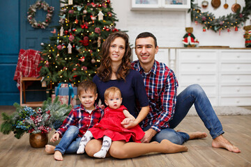 Happy family near fir-tree. Christmas celebration at home. Mom, Dad, son and daughter weared in blue and red. New year eve. Happy family in casual family look. Christmas decorated white interior