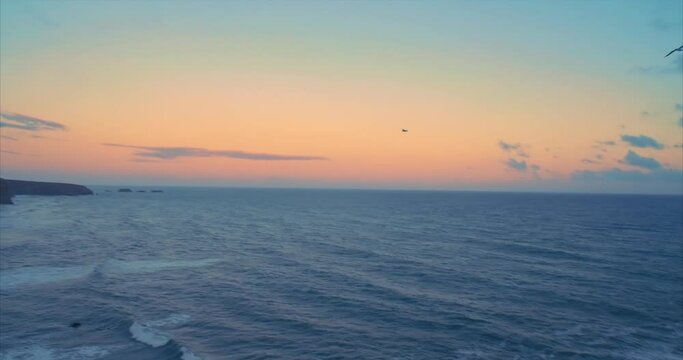 Aerial: Flying over ocean and rocky coastline at sunset. Bird flying in the sky. Annestown beach, Tramore, Ireland
