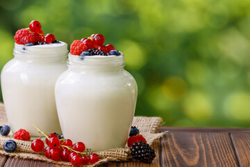 yogurt and fresh berries in two glass jars on table outdoors