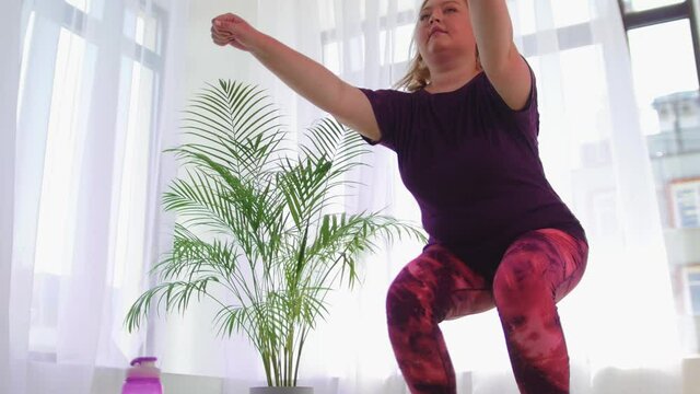 Fitness training - overweight woman squatting on the yoga mat in white room