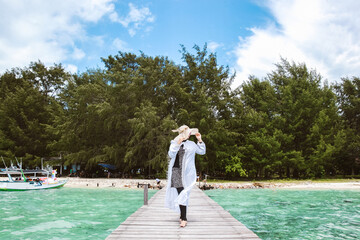 Woman tourist on vacation wearing white dress and summer hat posing on the wooden dock at Karimun Jawa island