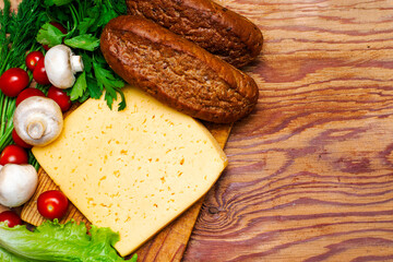 a piece of cheese greens lettuce cherry tomatoes mushrooms and rye buns on a wooden cutting board on the copyspace table