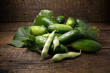 Cucumbers and string beans on a wooden background.Cucumber,dill and bean pods on a warm background of old boards.