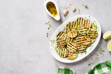 Grilled zucchini slices with garlic sauce in a white plate . Light gray stone background. Top view.