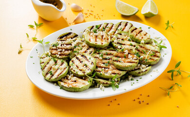 Grilled zucchini slices with garlic sauce in a white plate . Yellow background. 
