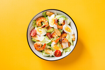 Fresh Shrimp Caesar Salad with parmesan cheese and Croutons. Yellow  background, top view.