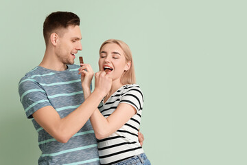 Young couple eating tasty chocolate on color background