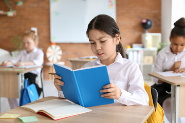 Cute little girl reading book during lesson at school