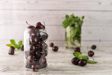 Ripe, juicy cherries in a glass glass close-up. A glass with mint sprigs in the background