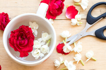 red rose, jasmine flowers float on the water in cup with scissors arrangement flat lay style on background wooden