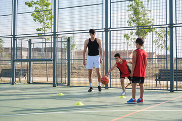 Two children learning how to play basketball, one of them has a leg prosthesis. Coach training two kids.