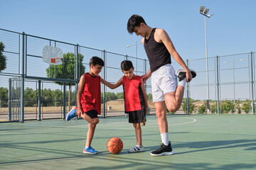 Basketball coach doing leg stretching exercises with two children, one of them has a leg...