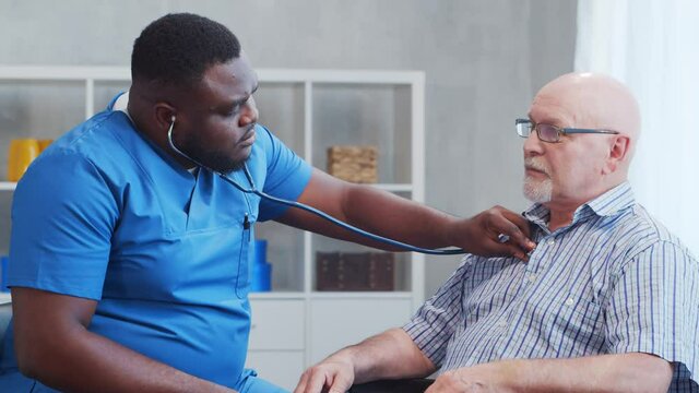 African-American caregiver and old disabled man in a wheelchair. Professional nurse and handicapped patient in a nursing home. Assistance, rehabilitation and health care.