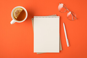 Top view photo of organizer pen glasses and white cup of tea with lemon slice on isolated vivid orange background with empty space