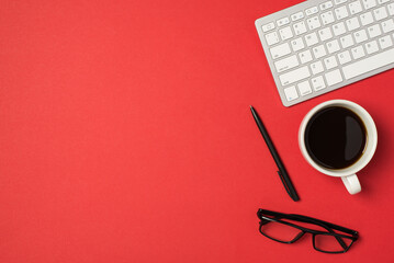 Top view photo of workspace white keyboard pen glasses and cup of coffee on isolated red background...