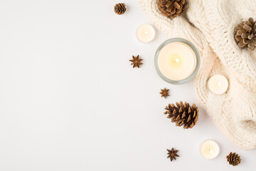 Top view photo of winter composition lighted candles white knitted sweater pine cones and anise on isolated white background with copyspace - obrazy, fototapety, plakaty