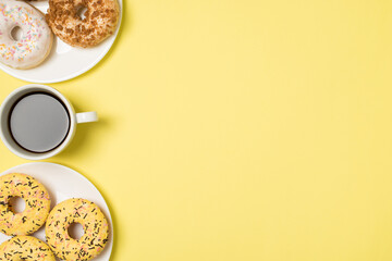 Top view photo of cup of coffee and two plates with different color glazed donuts on isolated pastel yellow background with copyspace