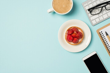 Top view photo of glasses on keyboard pen organizer plate with raspberry cake mobile phone and cup of frothy latte on isolated pastel blue background with copyspace