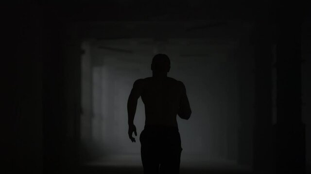 Fitness man running in dark corridor. Male jogger training in loft building