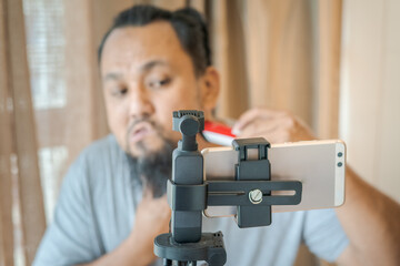 Asian man shaving beard with electric razor machine.