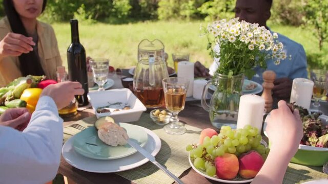Handheld shot footage of young multi-ethnic people spending time together outdoors sitting at table having delicious lunch