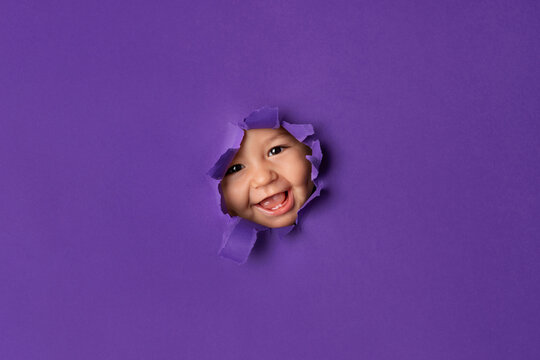 Smiling baby face peeking through purple torn paper