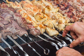 The man's hands are frying a shish kebab on the grill. Pork, chicken and lamb meat on skewers on the grill.