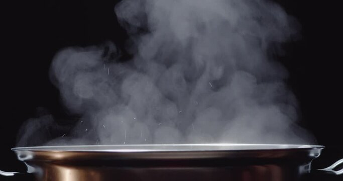 Slow motion of hot pot or shabu-shabu pot made of stainless steel, water boiling, hot steam rising on a black screen, hand using chopsticks to pick up a thin slice of pork put it into the pot.