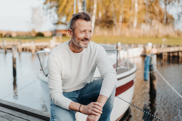 Active sporty man crouching in front of his yacht at the marina