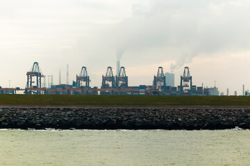 View from the bay to the container terminal with containers and container cranes against the background of the industrial zone.