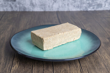 Halva, also Halvah or Halwa, Asian Turkish homemade sweet dessert made from fried sunflower seeds and sugar syrup served on a plate on a brown wooden background.
