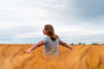 Happy girl having fun with outstretched arms in wheat field. Healthy young woman outdoors. Walking through field of rye