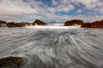 Sunrise at a beautiful beach with golden sunlight reflected on seawater and turbulent waves rushing onto the shore under dramatic dawning sky at Wai'ao Coast, Yilan ( Ilan ), Taiwan (Long Exposure)