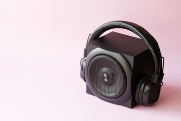 Black audio speaker and headphones on a pink background. The concept of pop music and acoustic...