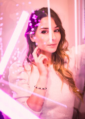 Beautiful young woman behind wet glass looking at camera with seductive gaze with pink led lights