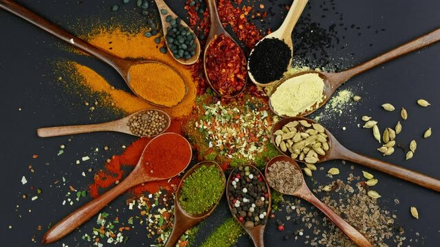 Dry colorful spices in spoons and bowls with fresh seasoning on dark background, top view