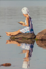 Young woman with a towel on her head at the sea. Lady reads a book in the water. The concept of summer outdoor recreation, relaxation. reading