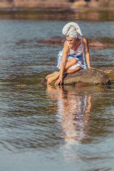 Young woman with a towel on her head at the sea. The lady touches the water with her hands. The concept of summer outdoor recreation, relaxation. good weather
