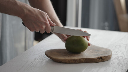 Man cutting ripe mango on olive board on white oak table