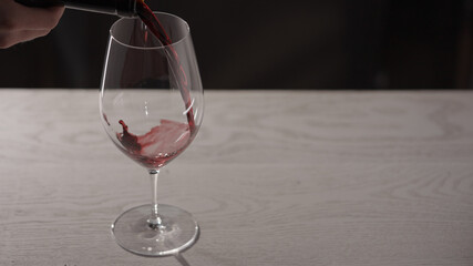 Pour red wine into wineglass on white oak table with copy space
