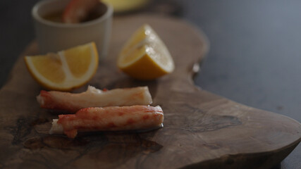 Crab leg meat on a olive board with sweet lemon and dip sauce on concrete countertop