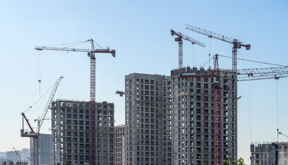 Construction cranes and unfinished residential buildings against clear blue sky. Housing construction, apartment block with scaffolding