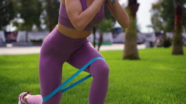 squats with elastic tape on legs, closeup of female legs during training outdoor