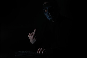 A man in a mask prints on the keyboard in the dark