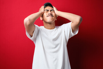 Young handsome asian man wearing white t-shirt with hand on head for pain in head because stress. Suffering migraine.