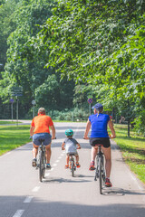 Family with kid or child cycling on the road bike in a park in summer, sustainable transport concept, vertical