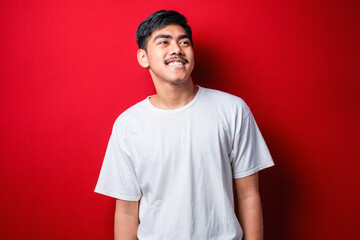 Young handsome man wearing white t-shirt looking away to side with smile on face, natural expression. Laughing confident.