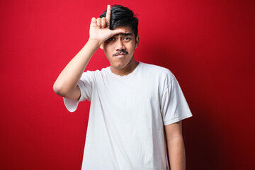 Fototapeta premium Young handsome man wearing white t-shirt making fun of people with fingers on forehead doing loser gesture mocking and insulting.